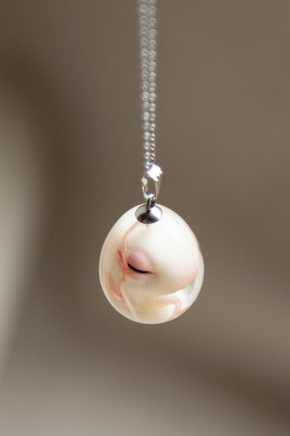 Small sculpture of a dragon embryo placed in an egg made of clear epoxy resin. Handmade pendant