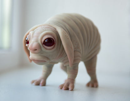 Pennsylvania squonk, mythical creature, cryptid. He is sad and cute, he has a fat body and clumsy legs with claws. Big eyes full of tears, a body with folds of skin, big ears. The sculpture is made of beige polymer, eyes are made of epoxy