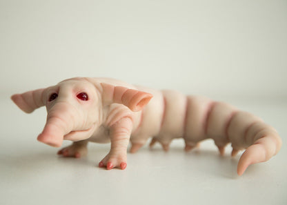 A fantasy character, an unusual hybrid creature of alien origin, an Elephant Grubb. It has the body of a larva with legs, and webbed paws in front, tubular ears and a trunk. The sculpture is made of beige polymer