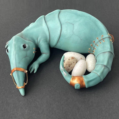 A fictional character, an alien reptile with elements of steampunk style, and 4 eggs. The creature has a long sharp nose and a narrow tail with spikes, two paws in front. On the body there are copper elements, a bracelet, brackets, a seam and a chain. The creature seems to guard its nest, next to it are 4 eggs covered with white and beige flock