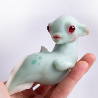 Turquoise alien fish with a transparent round crystal in its head. Its babies live in the transparent crystal. It has a beautiful face with slanted red alien eyes. This character was conceived, designed and realized in a small sculpture by our team of artists