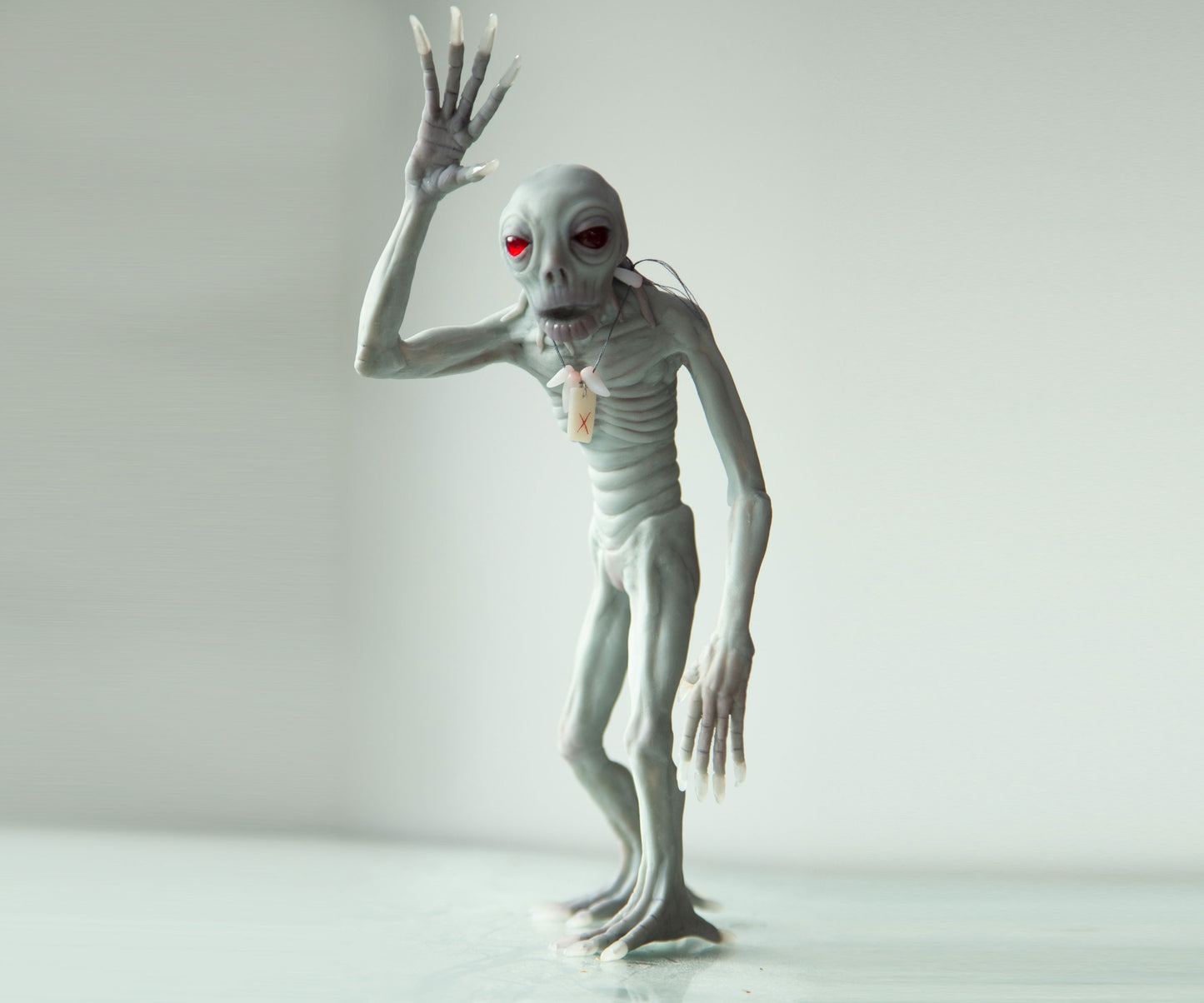 Skinwalker Gray alien-like figure with red eyes on a white background