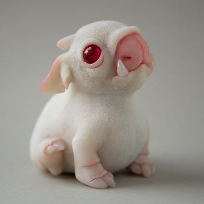 A cute fantasy alien puppy sitting on its hind legs. The figure is made of white polymer, has partial flocking, red transparent eyes and translucent claws. A unique character created by our team