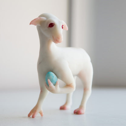 A fictional fantasy creature, an alien life form. It is a hybrid of a horse and a dragon. It has white skin, pointed ears like a goblin, and a face resembling a sheep. Its hind legs are like a horse's, and its front legs are like hands with fingers. It holds its blue egg with a baby to its chest with one hand.
