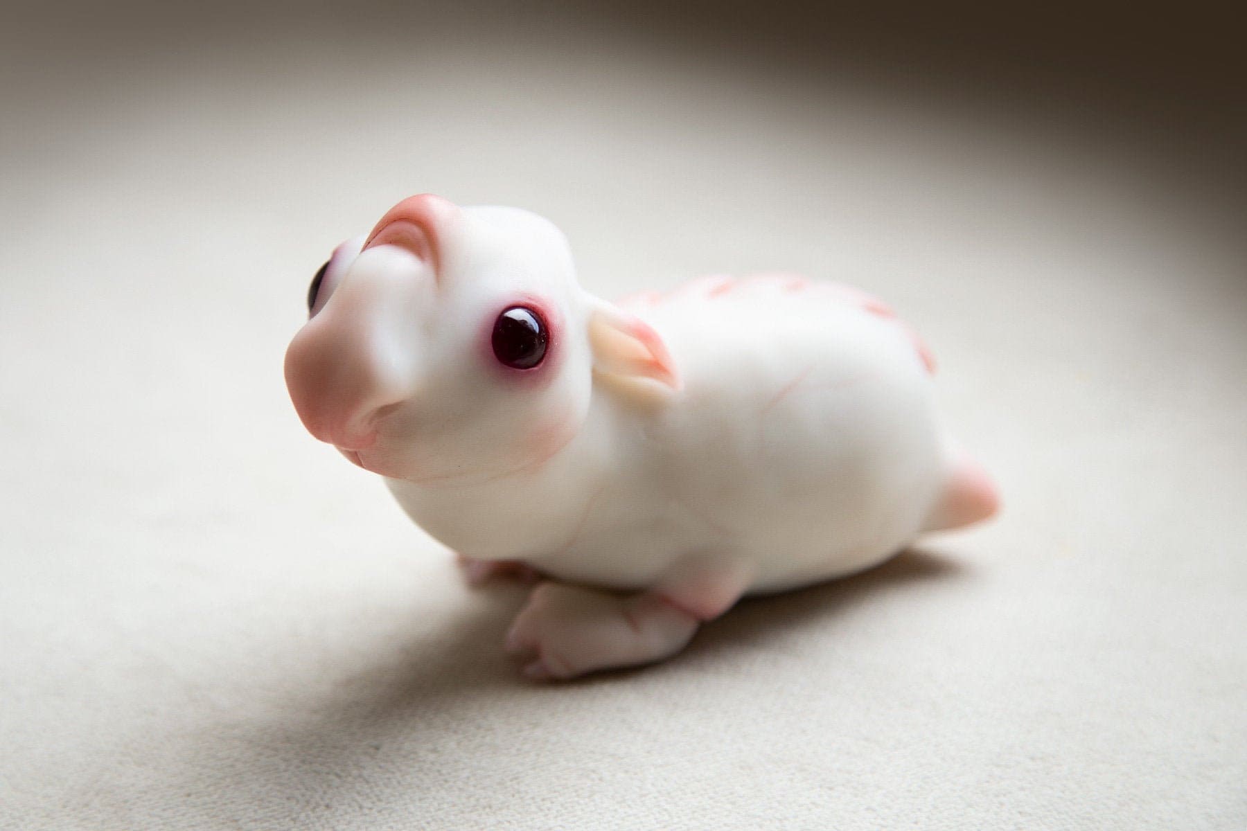 A fictional creature, an alien guinea pig - a hamster. It has a very cute face, red eyes, white skin and paws with claws. The sculpture is made of polymer, the eyes are made of epoxy resin