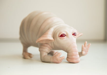 A cute alien animal, a sad algae eater. It has a fat body with folds of skin, hind legs with claws and hands in front. Large soft ears, a trunk for sucking up algae. If it eats stale algae, it poops colorful poop. The sculpture is made of beige polymer