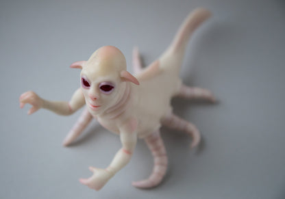 Sculpture of an alien from the water world, a hybrid of a human, a fish and an octopus. It has a human torso, arms, a head with red eyes, pointed ears and a human-like face. The body of a fish, on the sides there are tentacles, six of them. The skin is white, semi-transparent