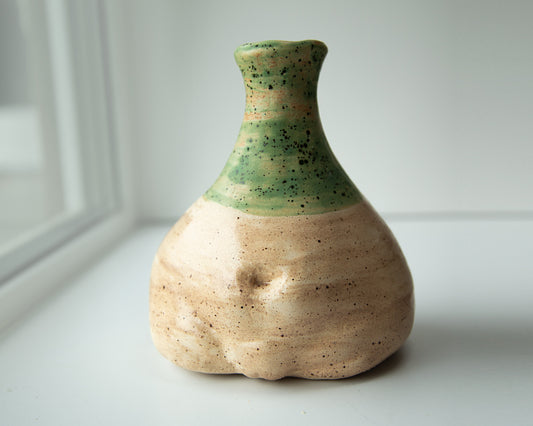 Rustic, sculptural, woman torso shaped, clay vase with earthy tones and a unique asymmetrical form, topped with a green glaze.