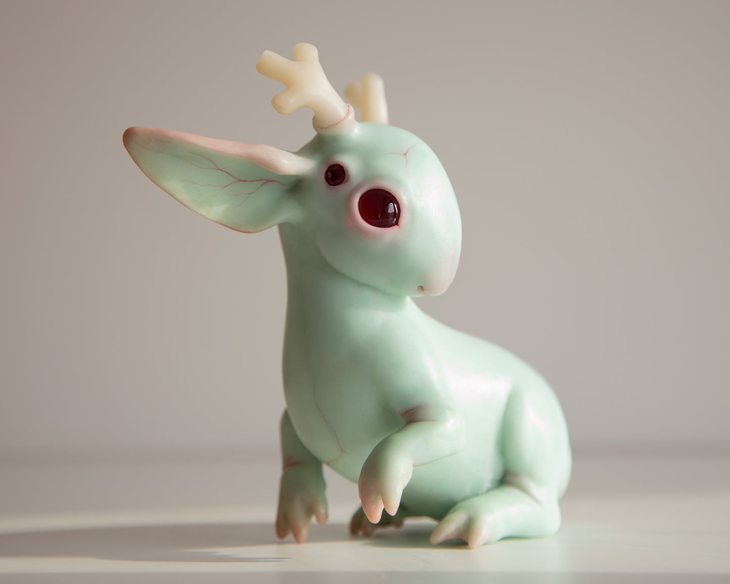 Jackalope cryptid Green creature figurine with large eyes and small antlers on a plain background