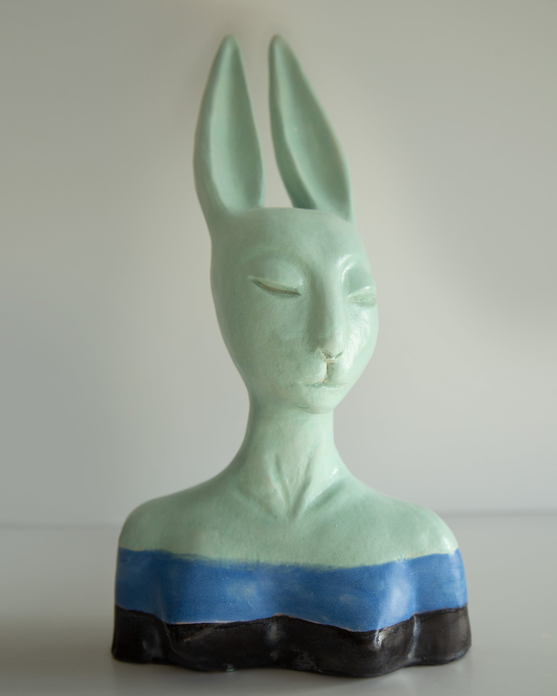 Green ceramic bust with rabbit-like features on a white background