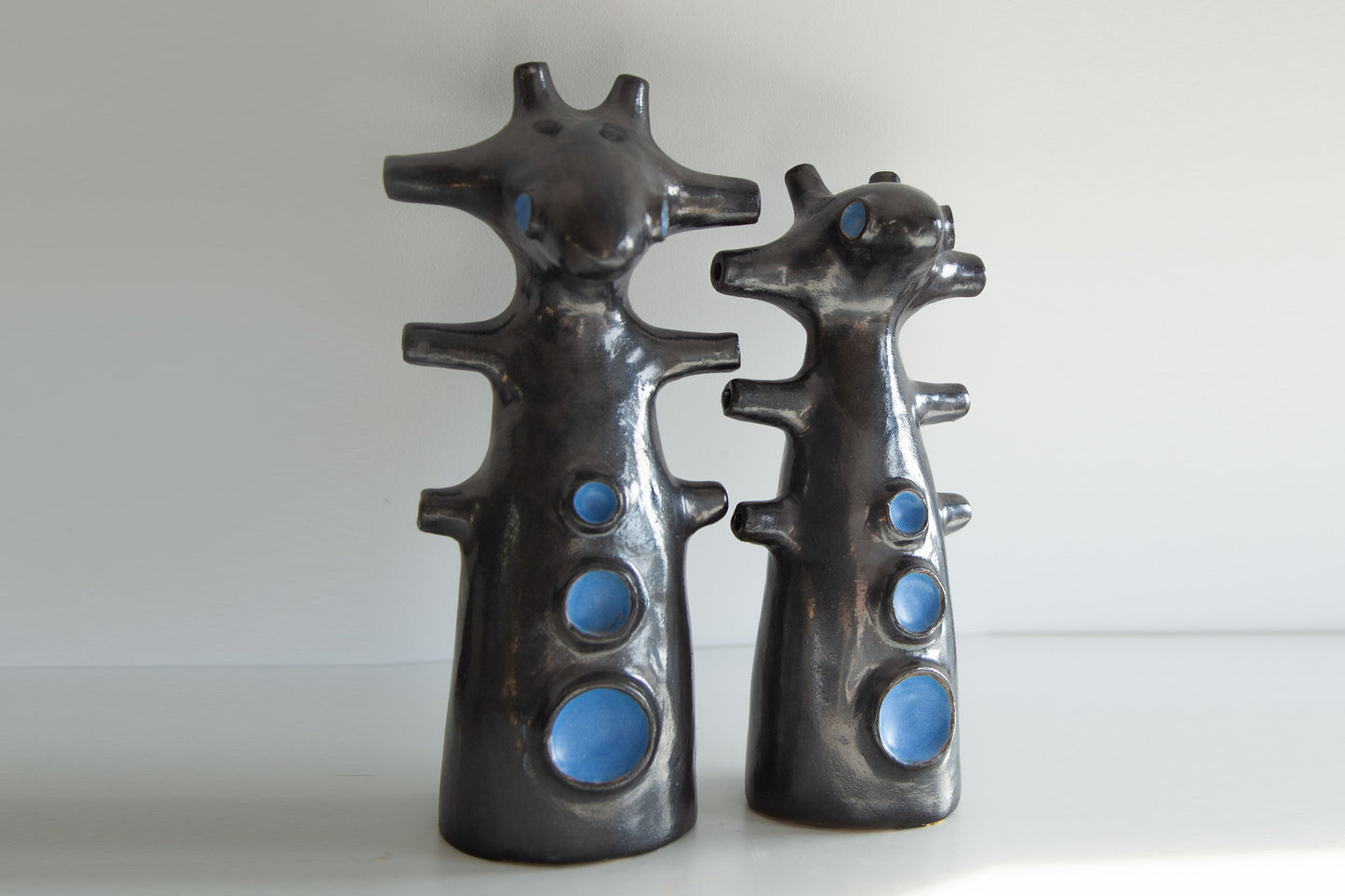 Two black ceramic figures with blue circular details on a white background