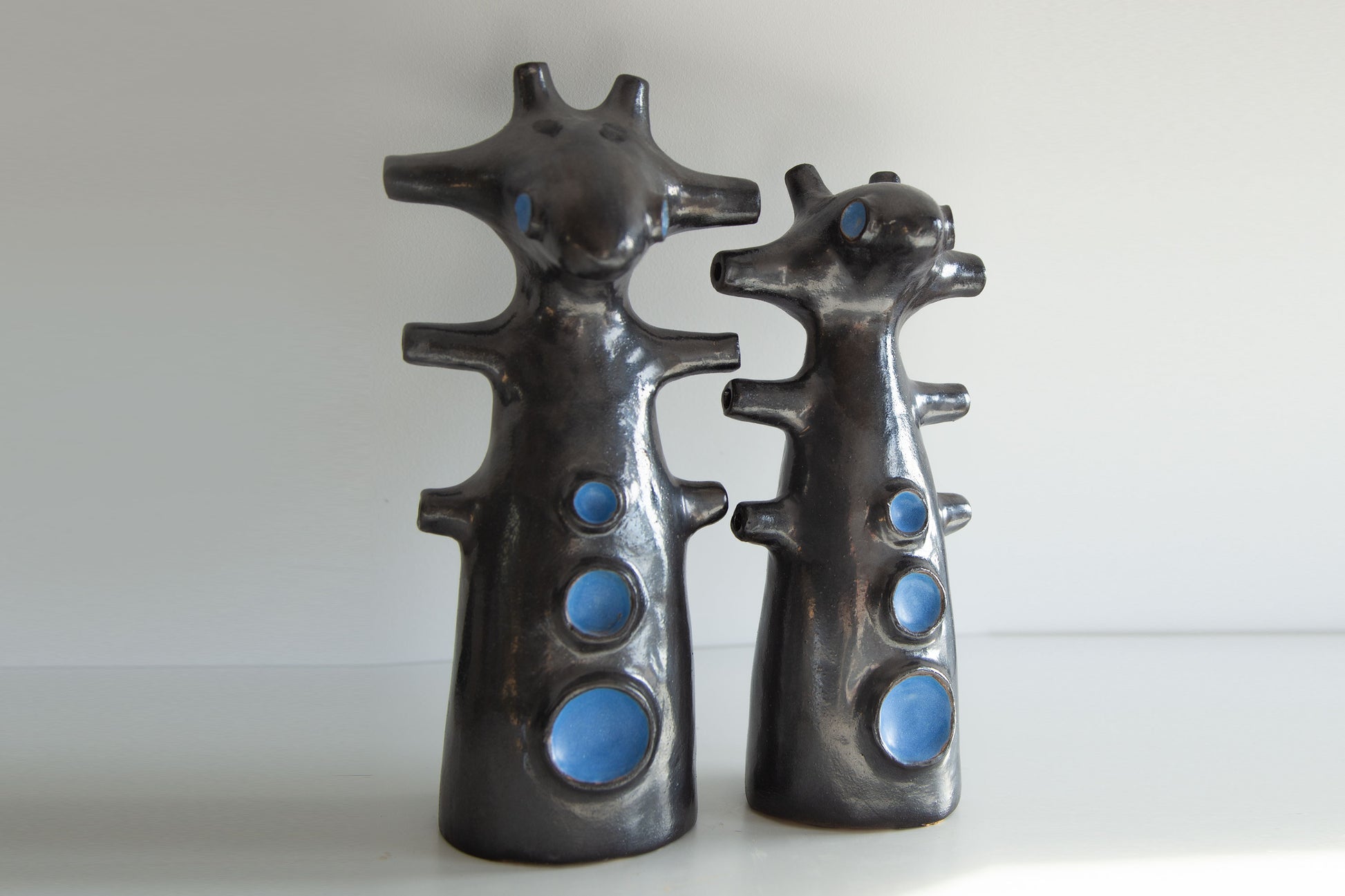 Two black ceramic figures with blue circular details on a white background