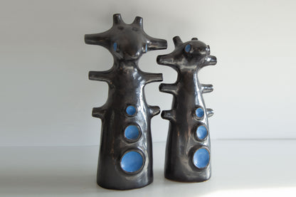 Two black ceramic figures with blue circular details on a white background