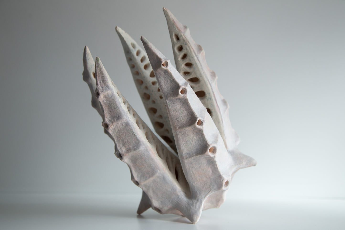 An abstract sculptural ceramic lamp with sharp, ribbed, leaf-like spikes and hollow perforations, shown on a neutral light gray background.