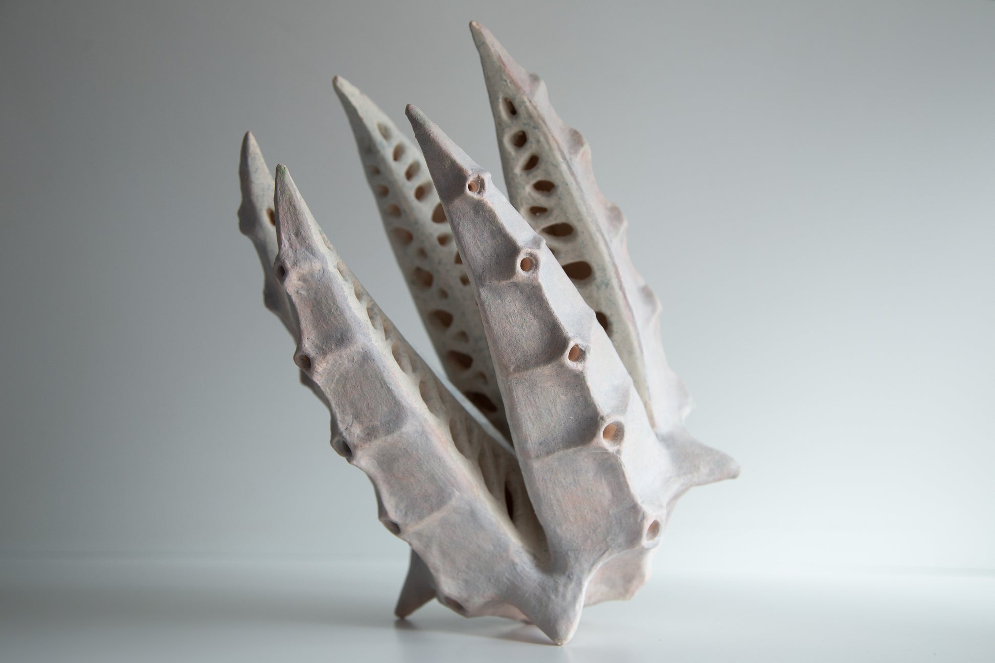 An abstract sculptural ceramic lamp with sharp, ribbed, leaf-like spikes and hollow perforations, shown on a neutral light gray background.