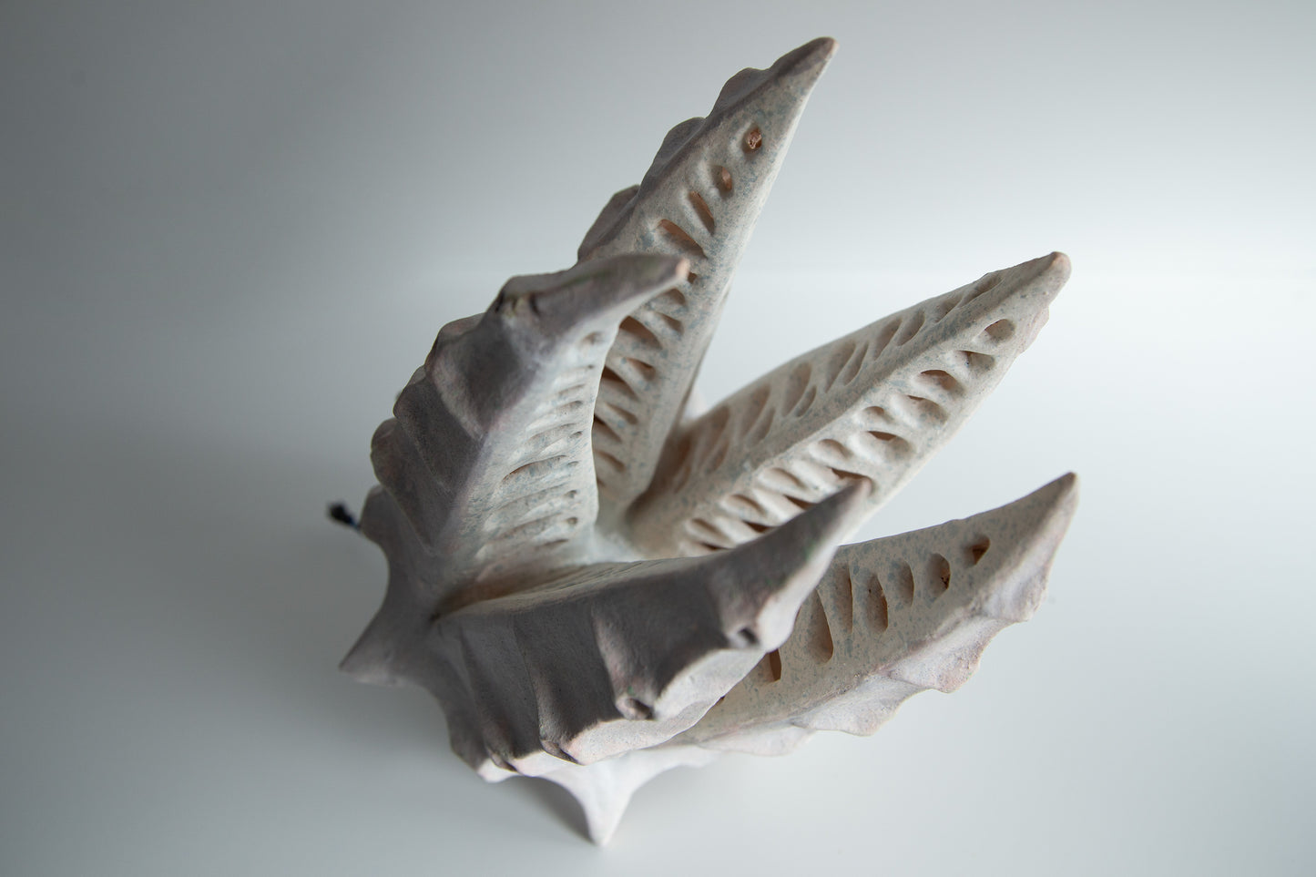 A sculptural ceramic table lamp shaped like stylized leaves, in a matte off-white glaze, photographed on a neutral light gray background.