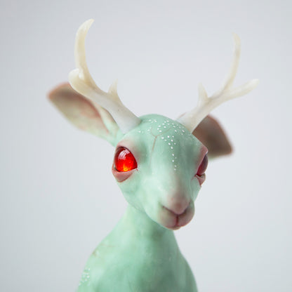 Sculpture of a rabbit with antelope horns, a mythical animal from the state of Wyoming. The rabbit is in a sitting position with its right paw raised up, ears - horizontally back. On the forehead are small horns with three branches. The sculpture is mint-colored, the horns are white translucent