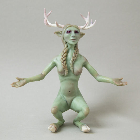 Handcrafted figurine of a mystical humanoid creature with green skin, delicate antlers, pointed ears, and long braided hair. The figure has an otherworldly appearance, blending human and animal features, with open arms and a serene expression.