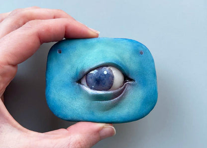 A small polymer sign with an eye. Wall decor. The eye is made realistically, with a blue pupil and a characteristic shine. There are two holes for hanging on the wall. An unusual handmade gift