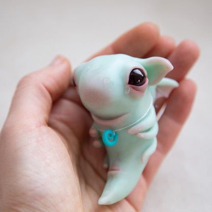 Small and cute baby dragon fantasy creature. Mint blue translucent body, red eyes, small dragon wings and 6 tiny tentacles. Aso it has necklace with blue pendant