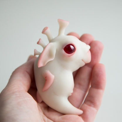 A small figurine of an alien seahorse. It has fins, horns and a cute face with a smile. Red eyes made of epoxy resin. This is a character we made up, the product is made of white translucent polymer