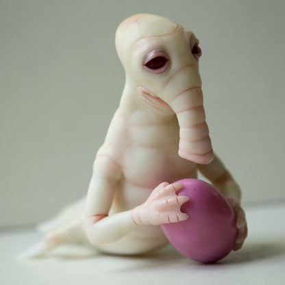 Fantasy alien creature, hybrid of humanoid, seal and elephant. He has albino appearence, hands and elephant like face. Also he holds pink egg in hands.