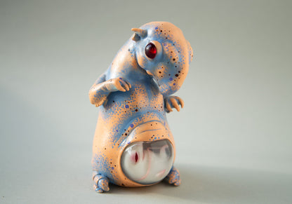 An alien creature, a pregnant tapir with a transparent belly in which a fetus is visible. This sculpture is hand painted in an abstract style. The ornament uses orange, blue, black and blue colors. The sculpture is made of acrylic and epoxy resin.
