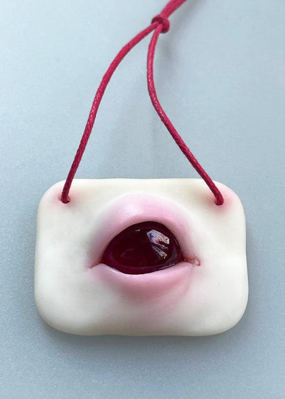 Red albino eye made from epoxy and polymer clay. a small plate with two holes for a rope for hanging, and a relief eye located in the middle of the plate