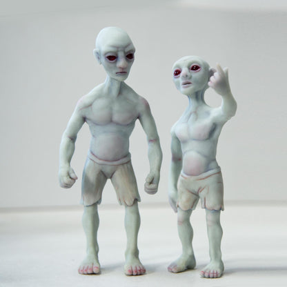 Melon Heads, mythical mutants from Connecticut urban legends. This is a sculpture of two mutant humans, they have blue-gray skin, dry, strong bodies, red eyes and melon-shaped heads. One figure is in a tense pose, arms at his sides, the other mutant is pointing at something in the distance.