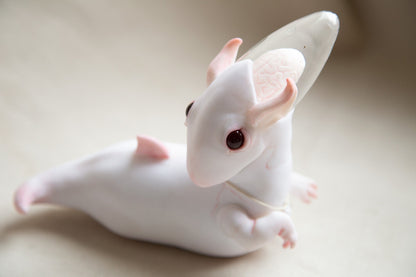 A gentle and surreal creature from the planet Cocoon. It has white, semi-transparent skin, red eyes, and small, pointed ears. The back of its head is crystal clear, revealing a highly developed brain. It has small paws in front, and its body ends in a finless tail.